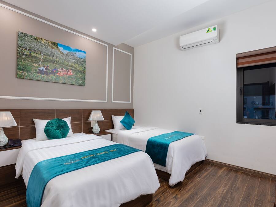 Ein Hotelzimmer mit zwei Betten, einem Bild an der Wand, einer Klimaanlage und einem Fenster.
