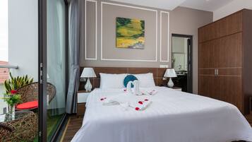 Une chambre d’hôtel avec un grand lit, deux tables de chevet avec des lampes, une armoire en bois, une porte en verre donnant sur un balcon et un tableau au mur.