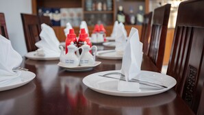 Una mesa de comedor dispuesta con platos blancos, cubiertos y botellas rojas de condimentos.