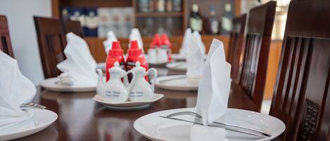 Une table à manger dressée avec de l’assiette blanche, des couverts en argent et des bouteilles de condiments rouges.