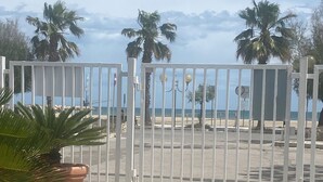 A gated entrance with a view of the beach and palm trees. - SoleeMare Barletta Apartments: Veranda Suite with Ocean View (Barletta)