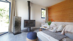 A modern living room with a wood-burning stove, a sofa, a coffee table, and a view of the outdoors. - Ty Kergui - Villa 400m from Tahiti sand beach (Névez)