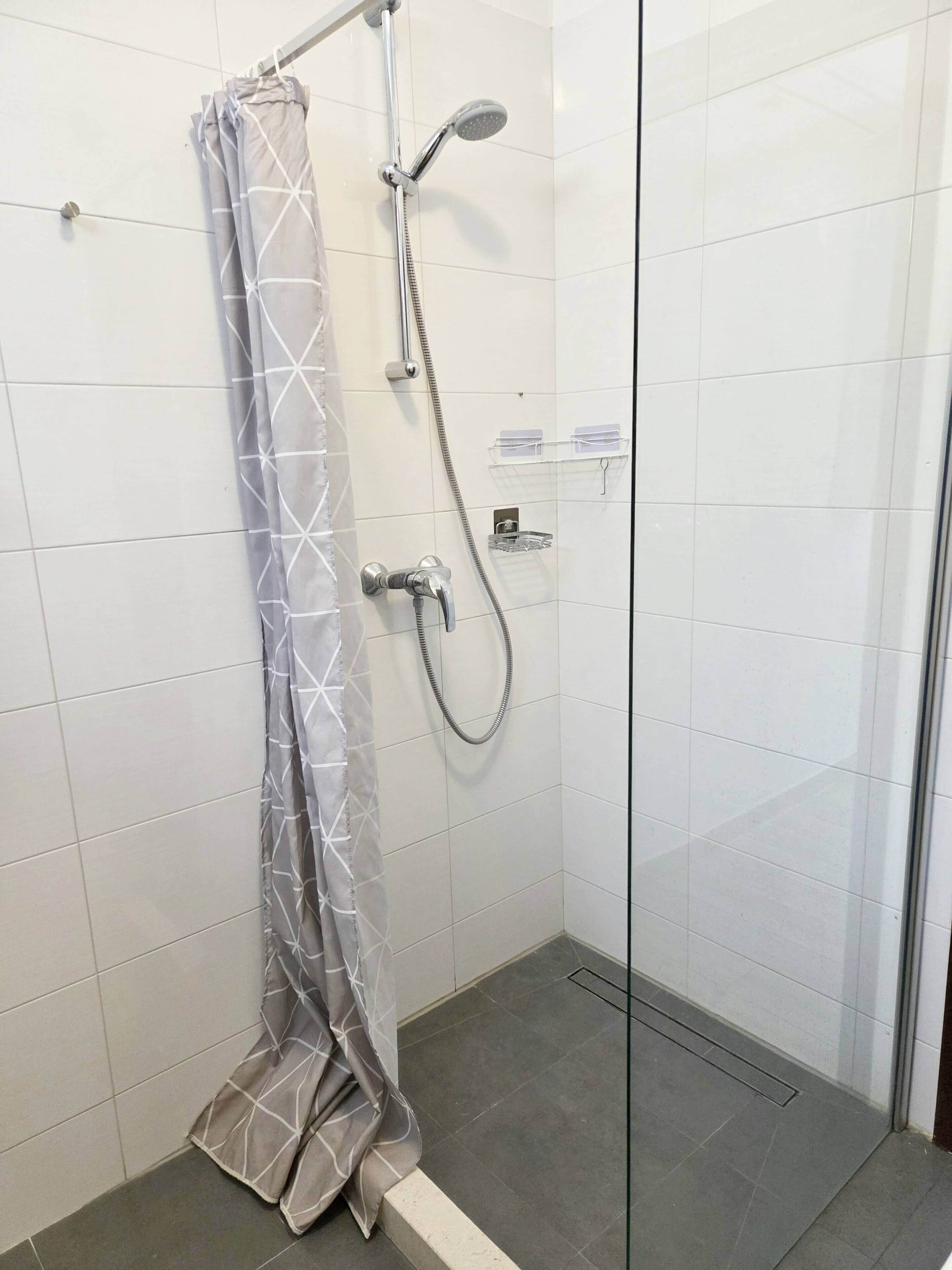 A shower with a grey patterned curtain, a handheld showerhead, and a wall-mounted control.