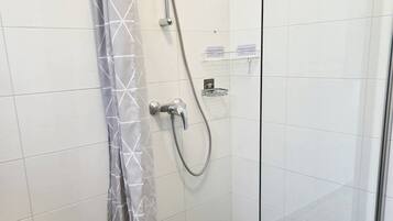 A shower with a grey patterned curtain, a handheld showerhead, and a wall-mounted control.