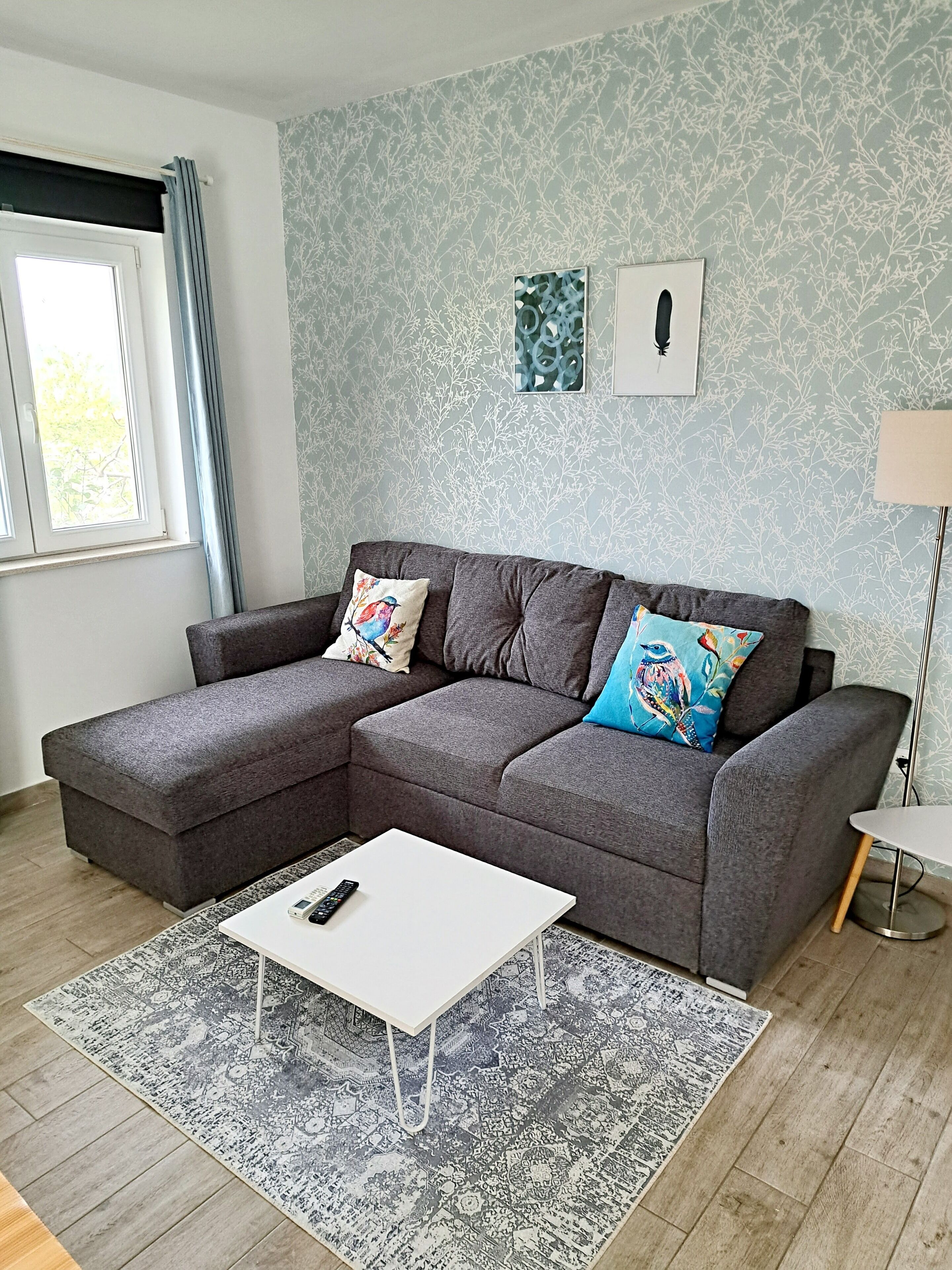 Een moderne woonkamer met een grijze modulaire bank, een witte salontafel en getextileerde vloerkleden.
