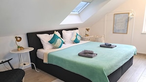 A modern bedroom with a skylight, a bed with a teal blanket, a bedside table with a lamp, and a small plant. - Adriatic Pearl Korcula (Korcula)