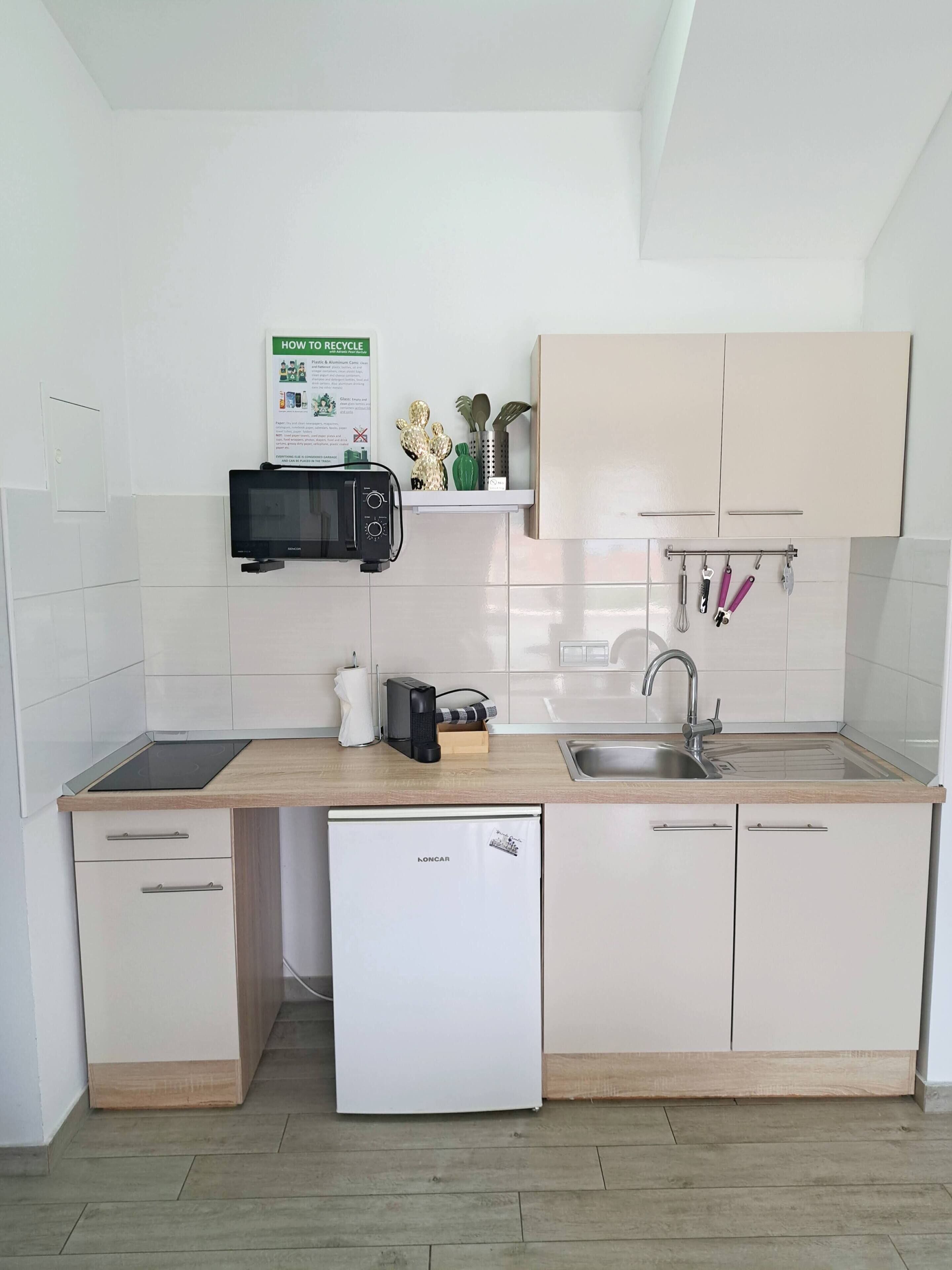 Una cocina compacta con microondas, tostadora, fregadero y un refrigerador pequeño.