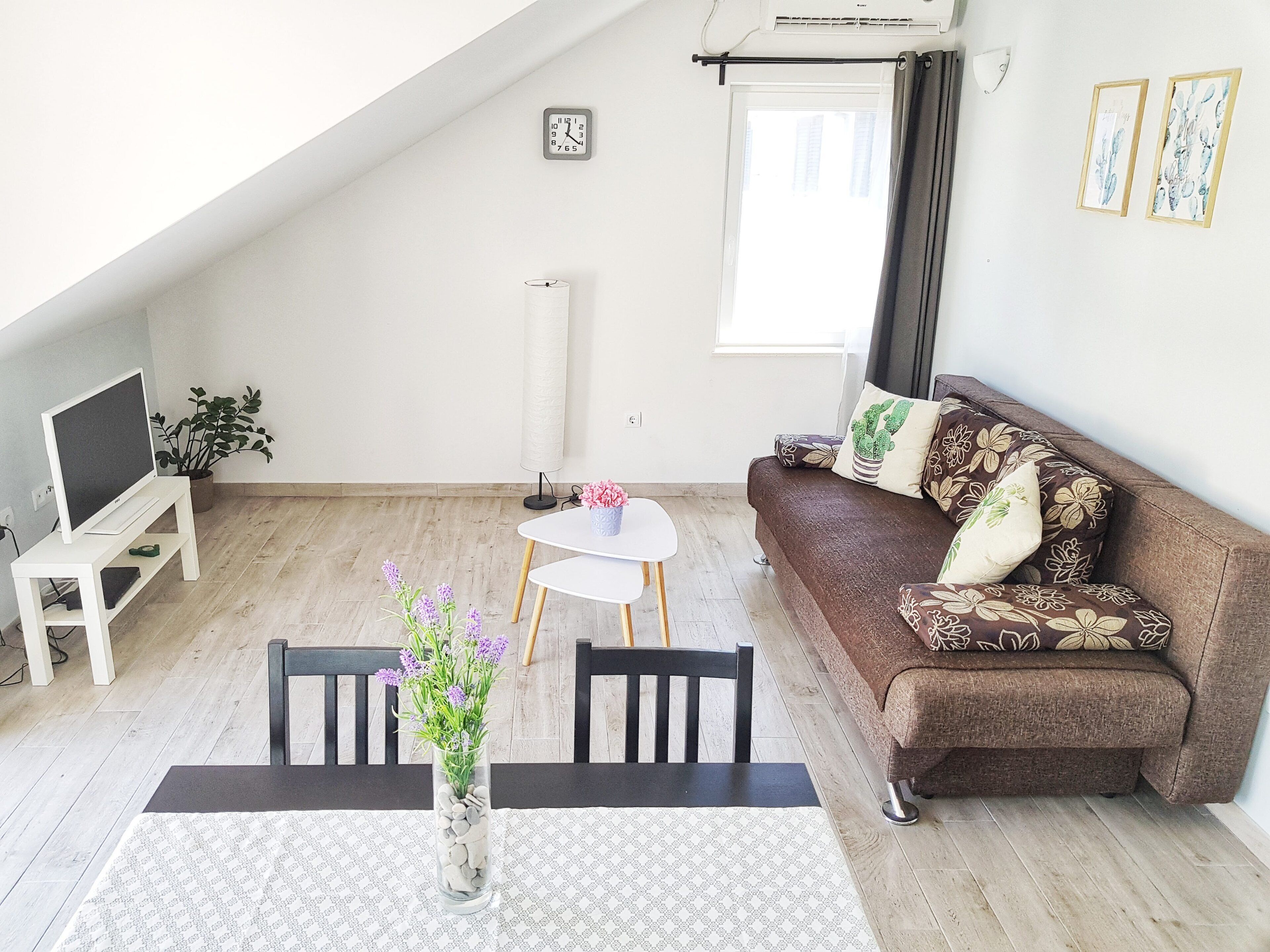 Un salon moderne avec un canapé marron, une table basse blanche et un téléviseur posé sur un meuble blanc.