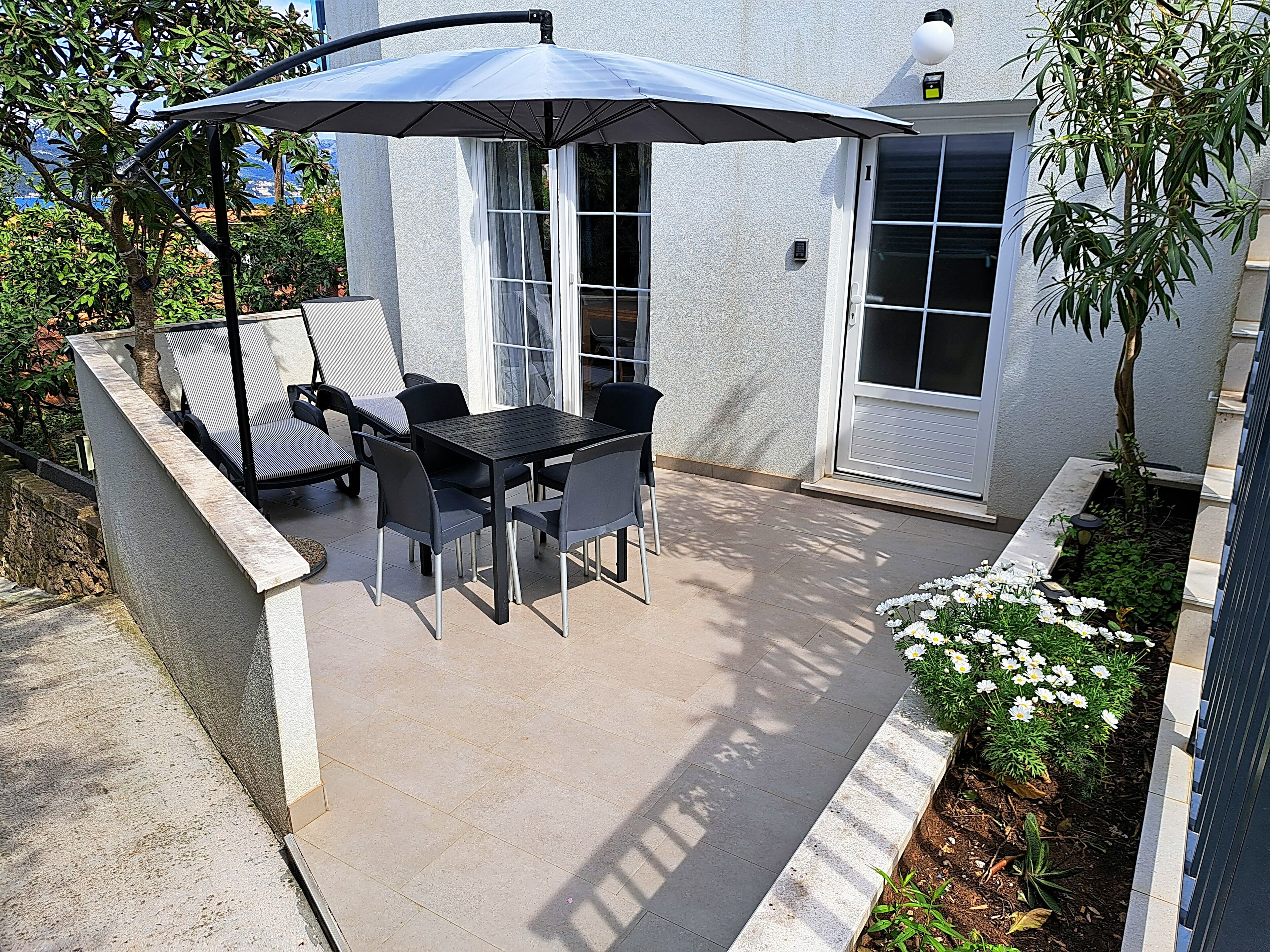 An outdoor patio with a table and chairs, a covered seating area, and a flower bed.