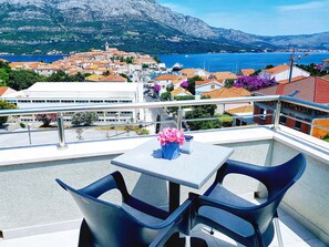 A balcony with two chairs and a table, overlooking a coastal town with buildings and a mountain in the background. - Adriatic Pearl Korcula (Korcula)
