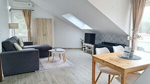A modern living room with a sofa, a small table, a TV, and a dining area with a wooden table and chairs. - Adriatic Pearl Korcula (Korcula)