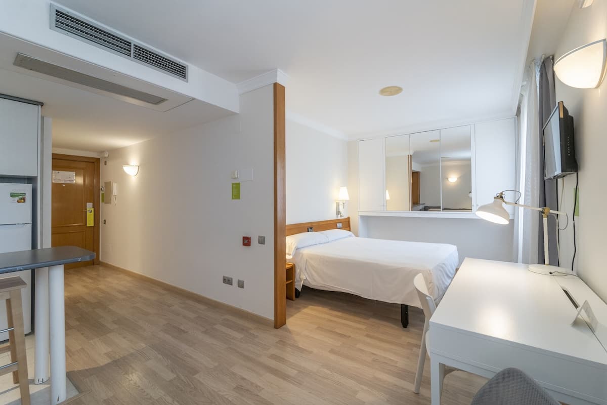 Une chambre d’hôtel avec un lit, un bureau, une chaise et un miroir.