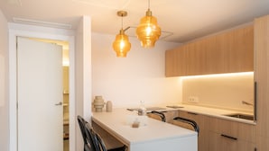 A modern kitchen with a central island, pendant lighting, and wooden cabinets. - ARTIEM Urban Apartments (Mahón)
