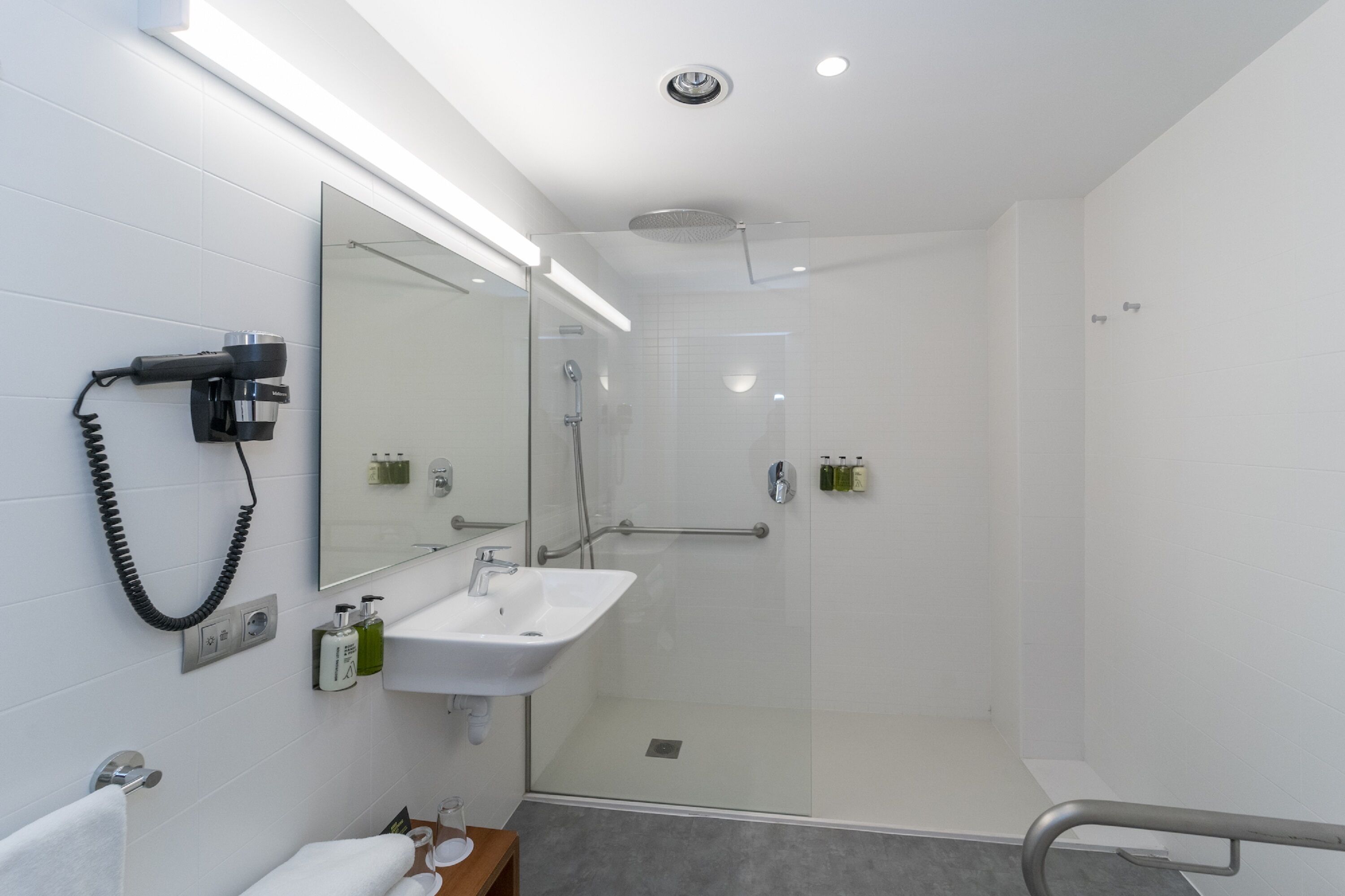 Une salle de bain moderne avec une douche à parois de verre, un lavabo blanc et un sèche-cheveux fixé au mur.
