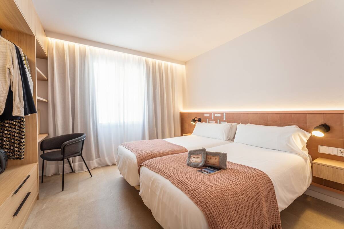 Une chambre d’hôtel avec deux lits, un bureau et une chaise.