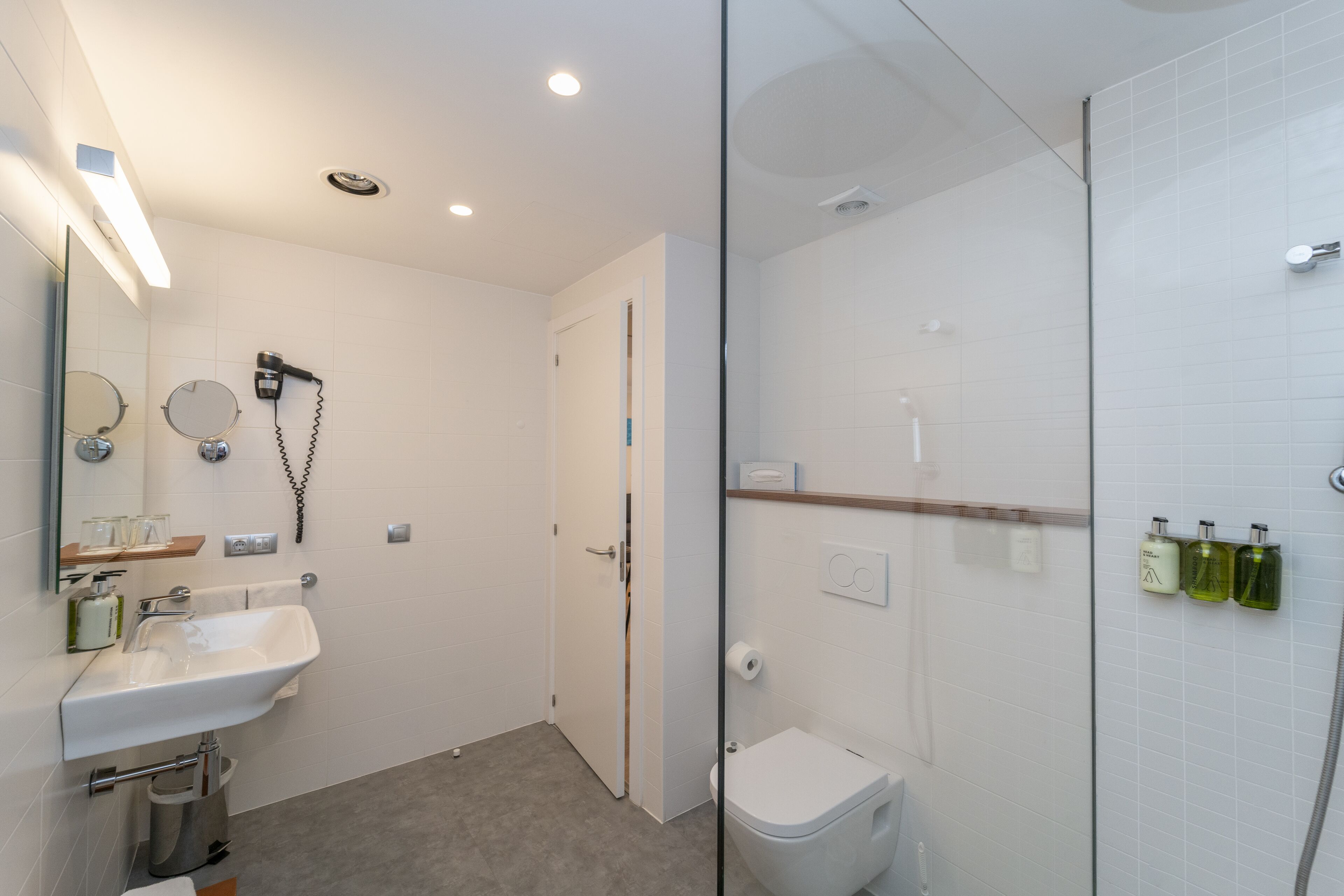 Een moderne badkamer met een douchecabine van glas, een witte wastafel met spiegel en toiletartikelen aan de muur.