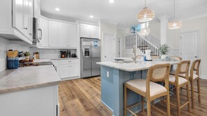 Una cocina moderna con armarios blancos, un refrigerador de acero inoxidable y una isla azul con taburetes de bar.