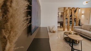 A modern living room with a flat-screen TV mounted on a textured wall, a sofa, a coffee table, and a staircase leading to an upper level. - Mix of modern and antique , New visage villa Antico (Seget Donji)