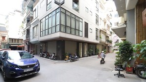 A modern building with a corner entrance, a parked blue car, and several motorcycles. - Stay Kim Ma Hotel (Hanoi)