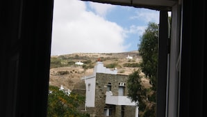 Vista desde una habitación que se abre a un edificio blanco con muros de piedra, un camino de piedra y una colina al fondo.