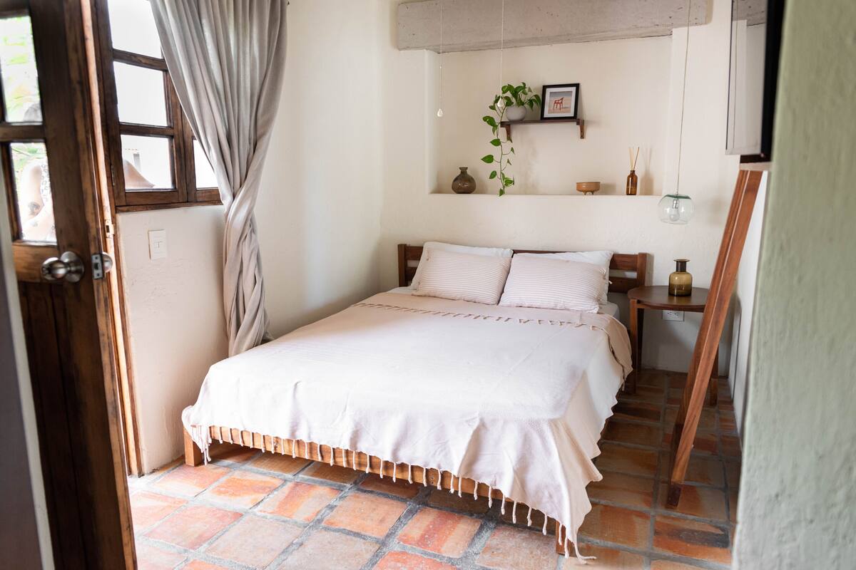 A bedroom with a bed, a nightstand, a dresser, a mirror, and a potted plant.