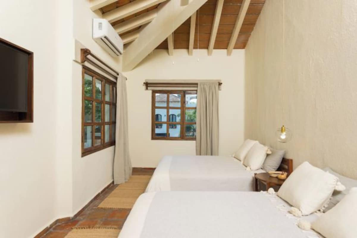 A bedroom with two beds, a TV, and a window with curtains.