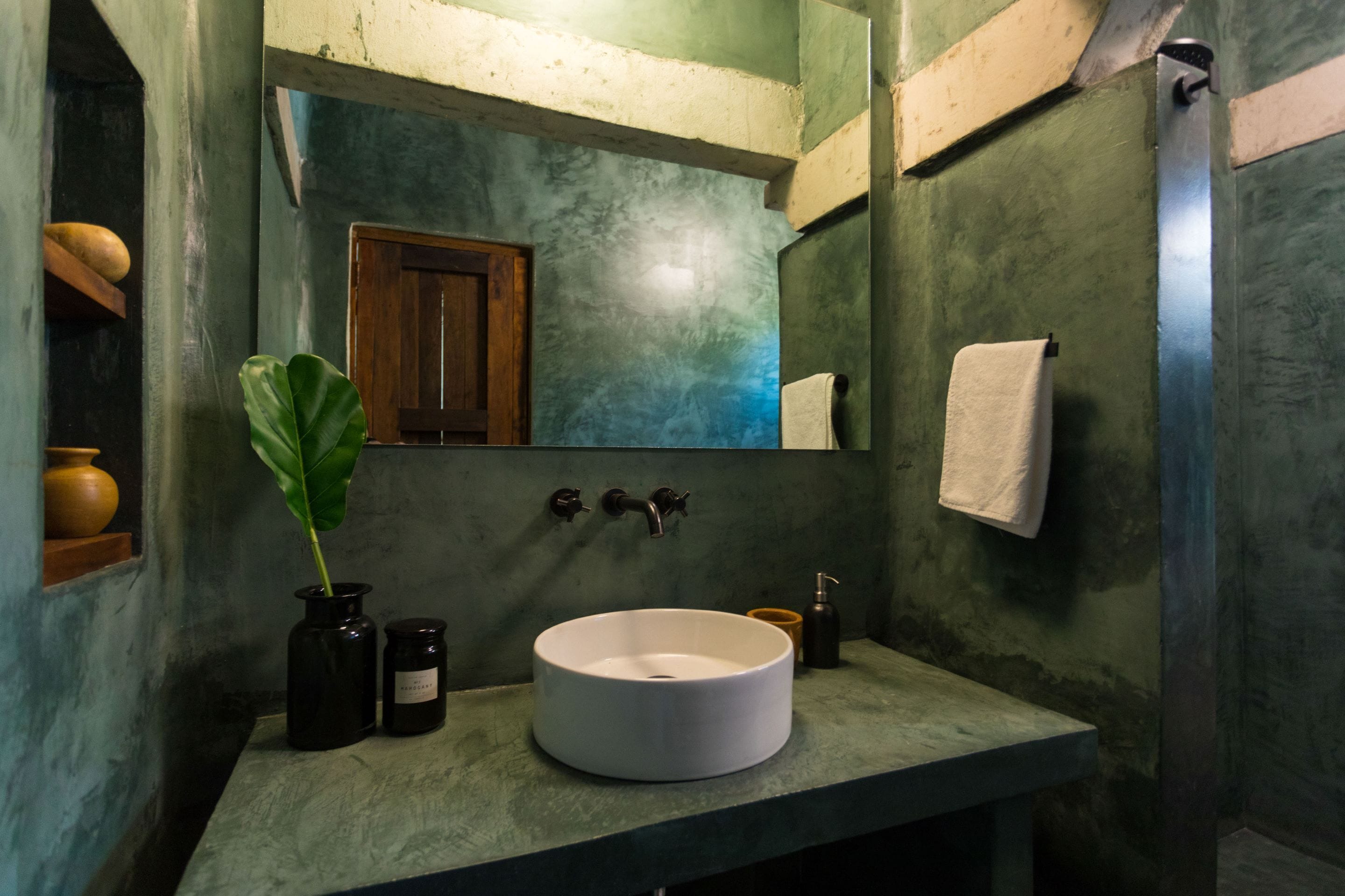 A bathroom with a round sink, a mirror, a wooden door, and a towel hanging on the wall.