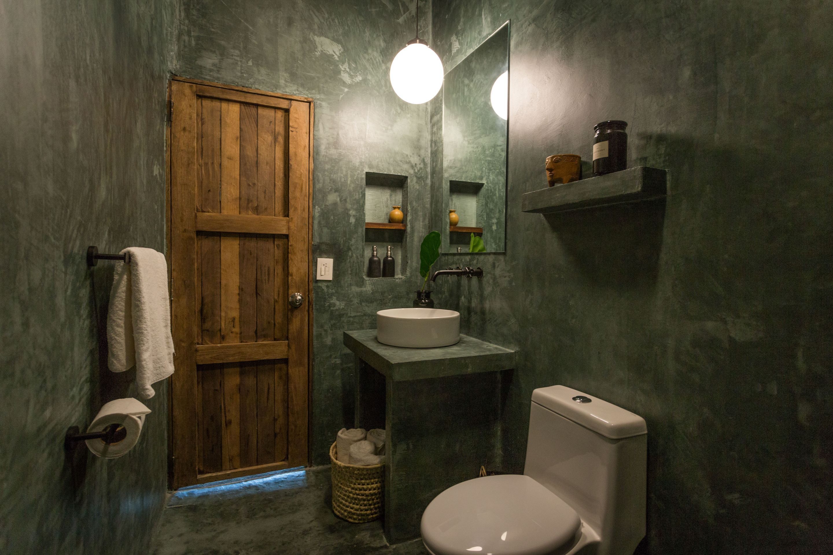 Un baño con puerta de madera, un espejo redondo, un lavamanos y un inodoro.