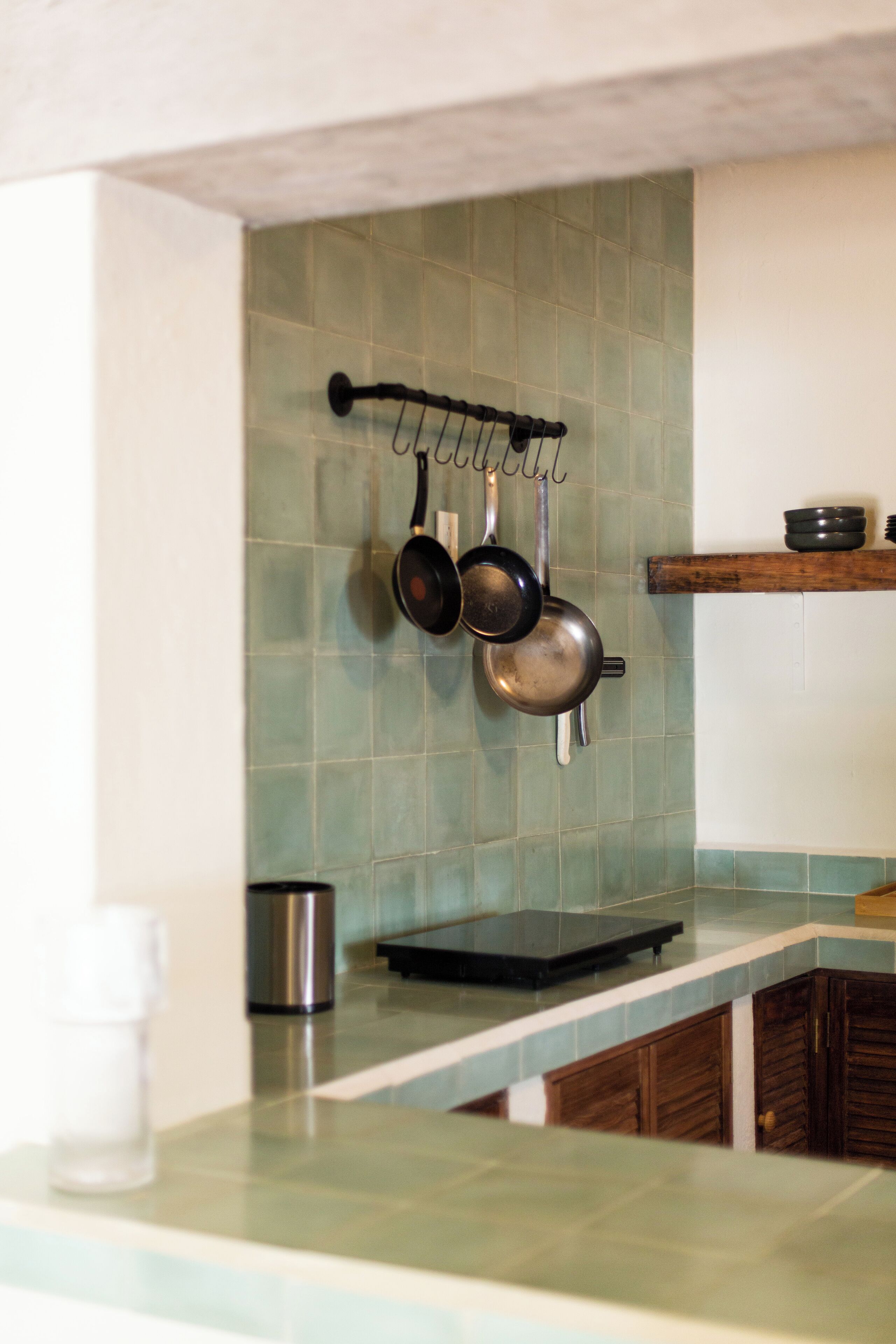 A kitchen with a hanging pot rack, a stainless steel kettle, and a wooden shelf.