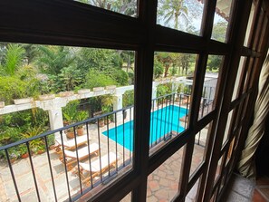 A view through a window of a pool area with a white fence, potted plants, and lounge chairs. - Casa Ritual (Puerto Vallarta)