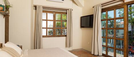 A bedroom with a bed, a TV, a window, and a door leading to a balcony.