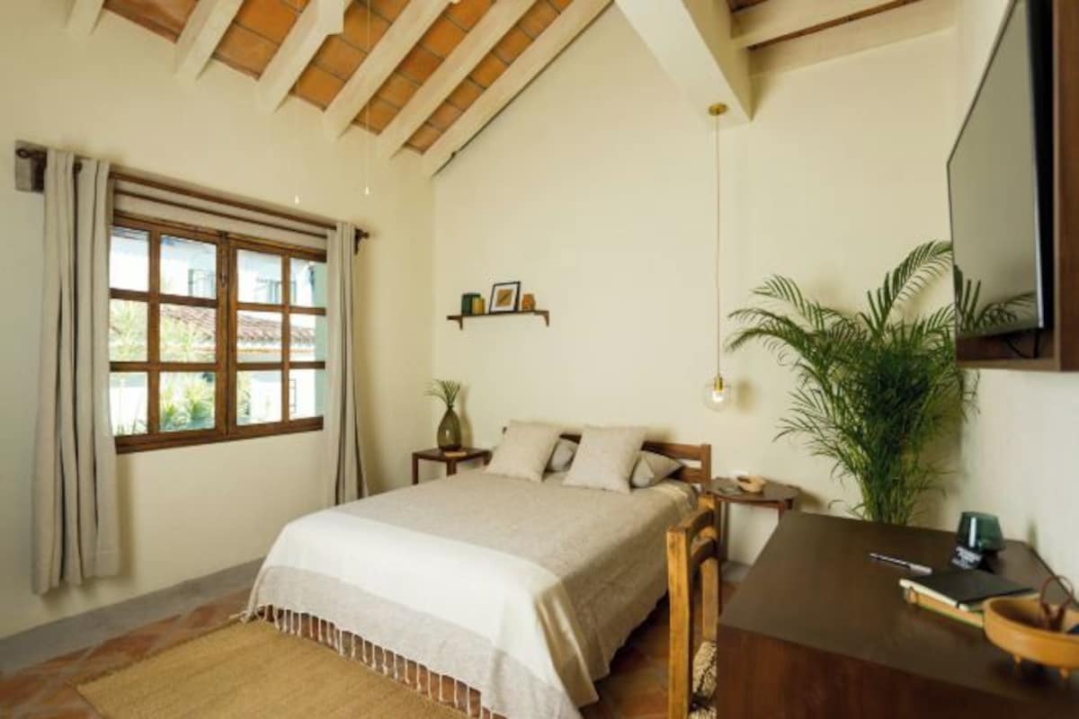 A bedroom with a bed, bedside tables, a desk, a mirror, and a large window with curtains.