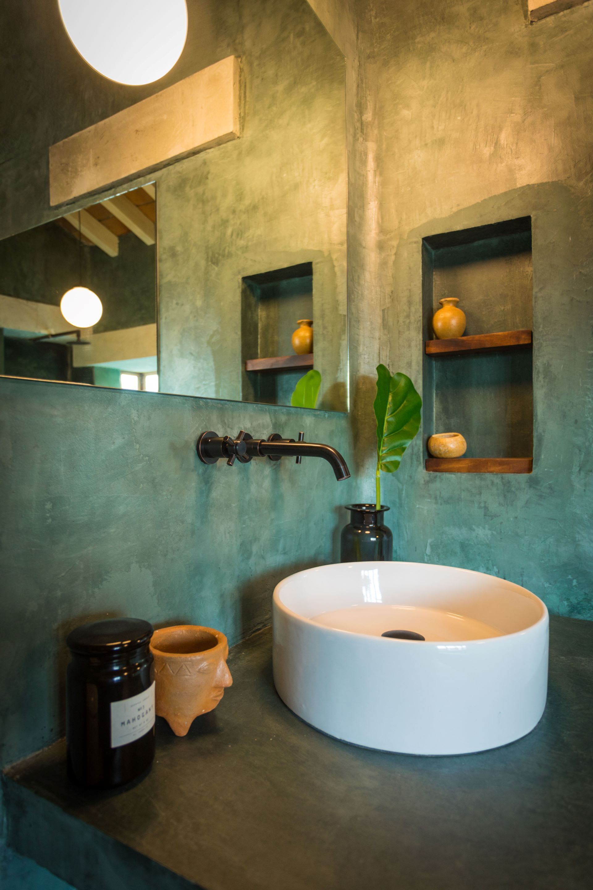 Ein Badezimmer mit einem runden, weißen Waschbecken, einem schwarzen Wasserhahn, einem Spiegel und einem Regal mit einer Vase und einer Pflanze.