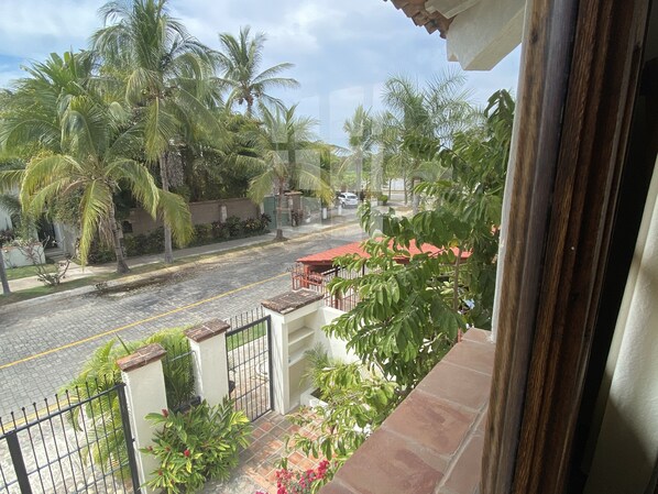 A balcony with a view of a street lined with palm trees and a red-roofed building. - Casa Ritual (Puerto Vallarta)