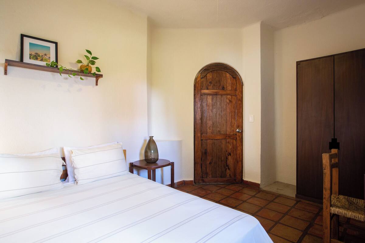 A bedroom with a bed, a wooden door, a wardrobe, and a small table with a vase.