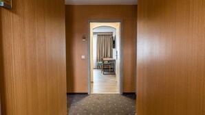 Un pasillo con paredes de madera y suelo alfombrado que conduce a una habitación con una cama, una silla y una mesa.
