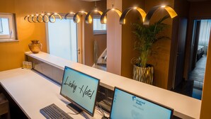 Una recepción de hotel con dos monitores de computadora mostrando el nombre del hotel y una planta cercana.