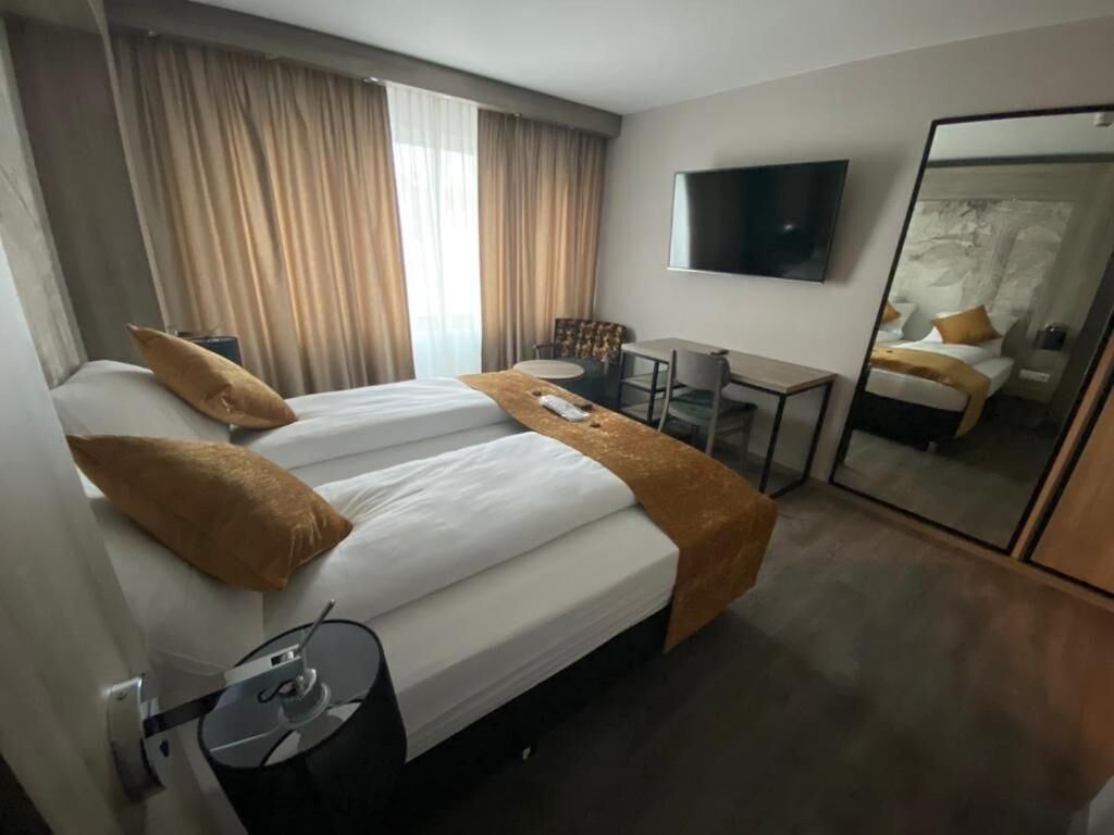 A hotel room with two beds, a desk, a chair, a TV, and a large mirror.