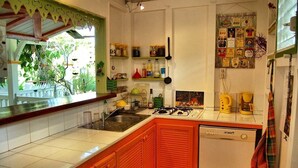 A kitchen with a gas stove, sink, and a dishwasher. There are shelves with jars and bottles, and a window with a view of greenery.