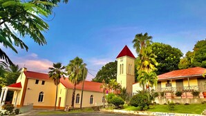 A church with a red roof and a clock tower, surrounded by palm trees and a clear sky. - Villa Mabouya (6 pers.) (Deshaies)