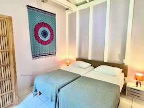 A bed with two pillows, a bedside table with a lamp, and a wall tapestry. - Villa Mabouya (6 pers.) (Deshaies)