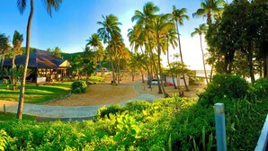 A resort with a covered area, palm trees, and a pathway leading to the beach.