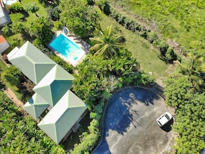 An aerial view of a property with a swimming pool, a curved driveway, and a car parked on the street. - Villa Mabouya (6 pers.) (Deshaies)