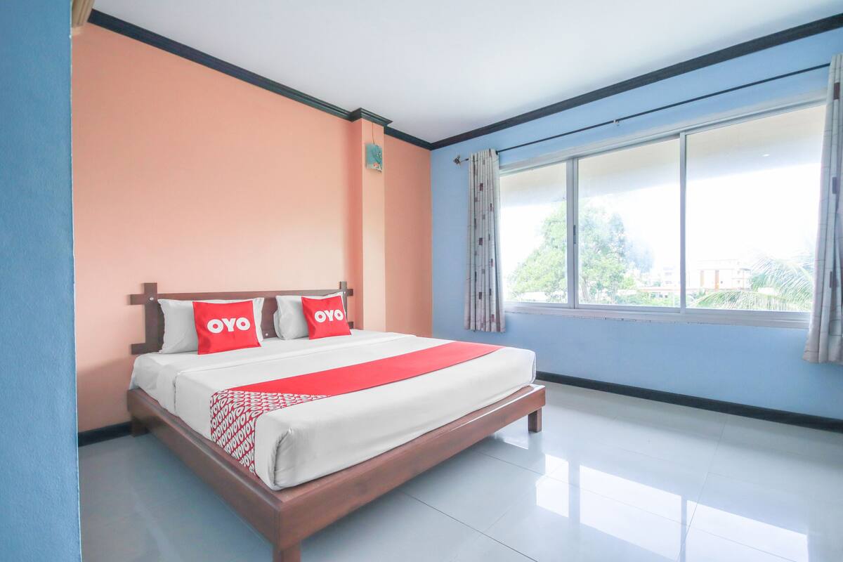 A neatly made bed with a red and white bedspread, two pillows with the word "OYO" on them, and a window with curtains.