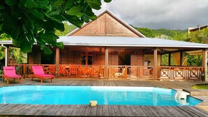 Una cabaña de madera con piscina, que cuenta con una terraza techada y sillas de descanso.