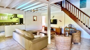 Amplia sala de estar con sofá, sillones de mimbre, televisor y una escalera.