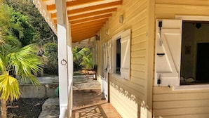 A covered outdoor area with a tiled floor leading to a building with multiple windows and doors.