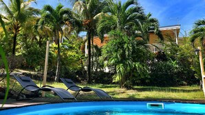 A swimming pool with lounge chairs, surrounded by palm trees and a building in the background.