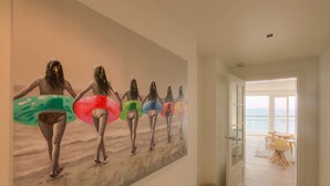 Un corridoio con un grande murale raffigurante persone che reggono tavole da surf colorate, che dà su una vista sulla spiaggia attraverso un'apertura.