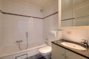 Ein Badezimmer mit weißen Fliesen, einer Badewanne, einer Toilette, einem Waschbecken und einem Spiegel.